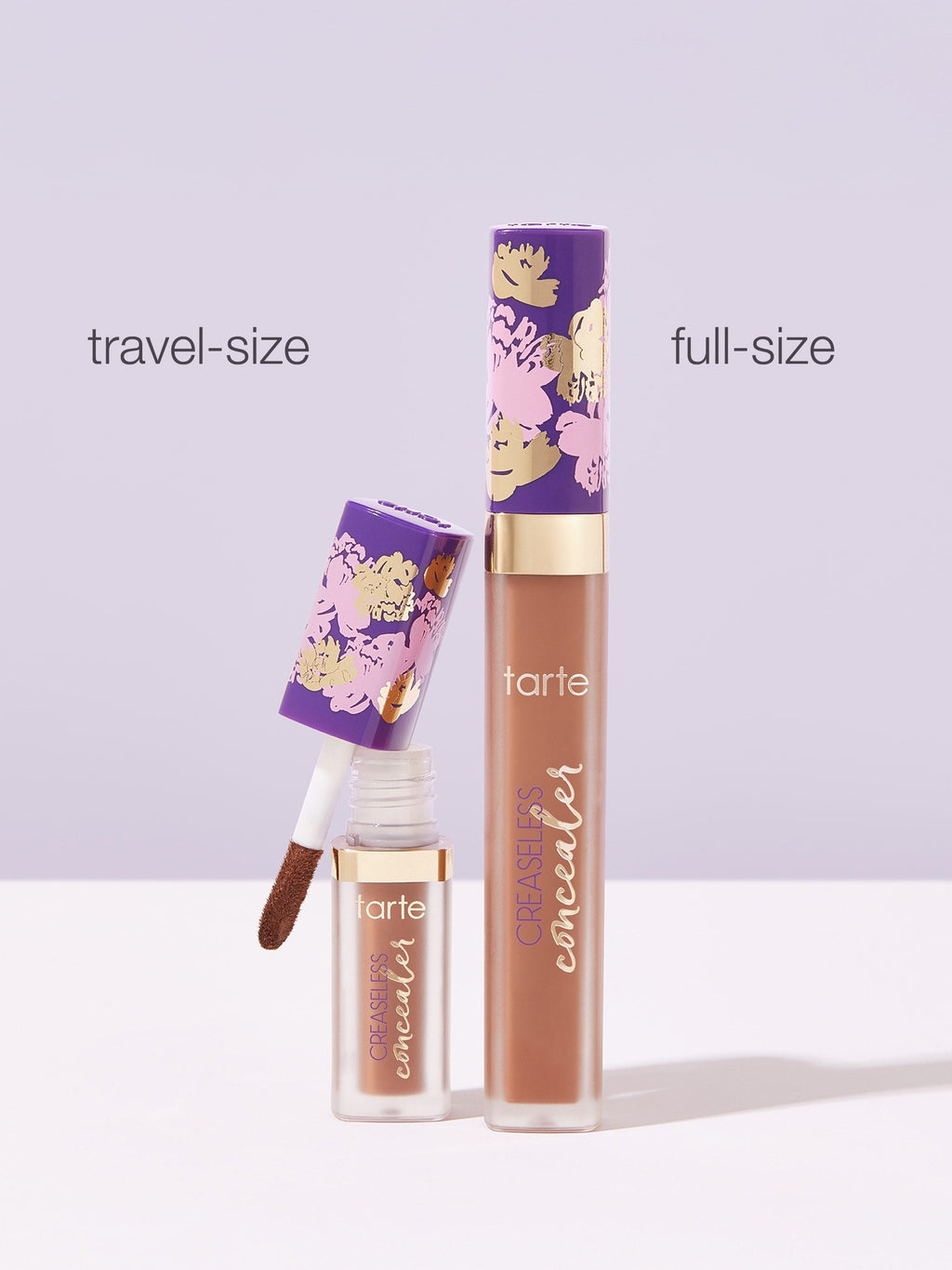 Two Tarte Cosmetics concealers, one travel-size and one full-size, stand against a light purple background. The smaller one is open, displaying the applicator; both tubes have floral designs. Text: travel-size, full-size, tarte, CREASELESS concealer.